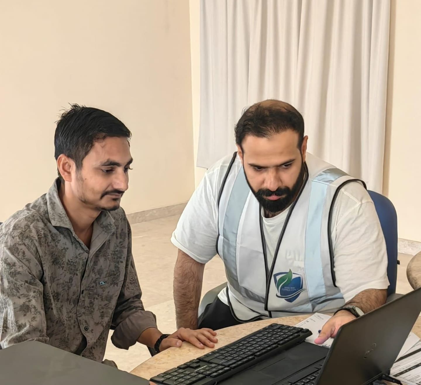 A KADI consultant in a high-visibility vest going through HSE training material on a laptop with an MBBT team member.
